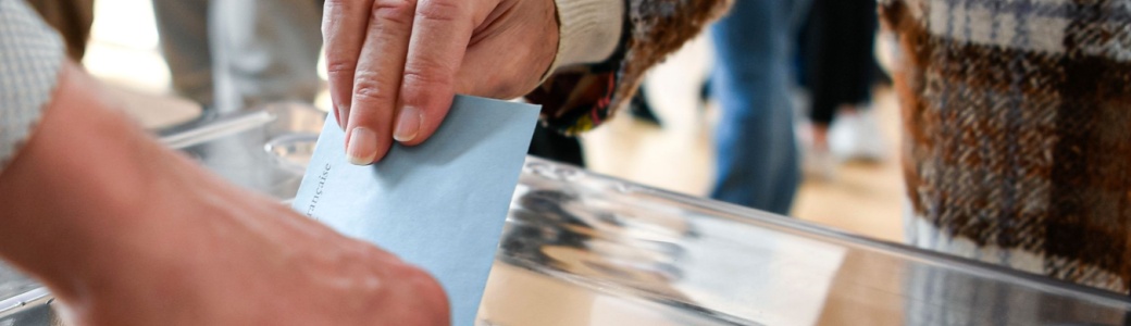 A person putting a ballot paper into a box.