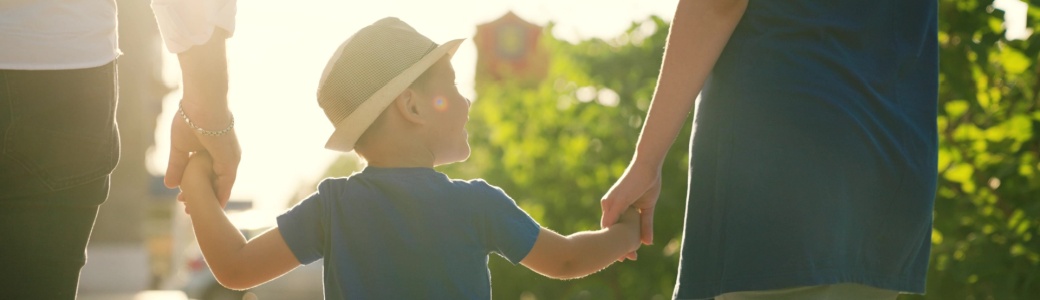 A family with a young child holding hands outdoors.