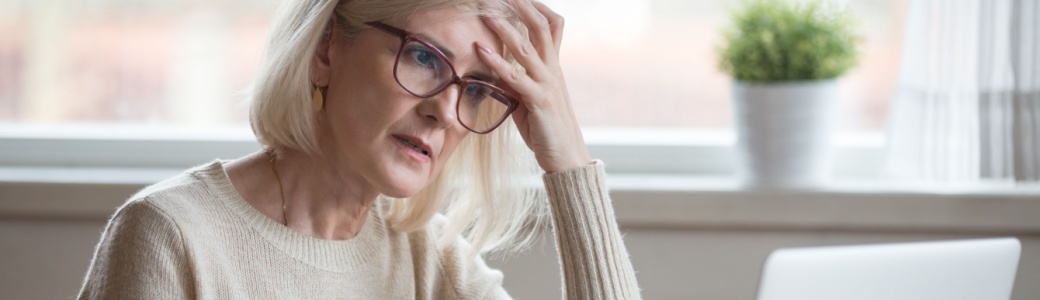 A retired woman looking worried while using a laptop.