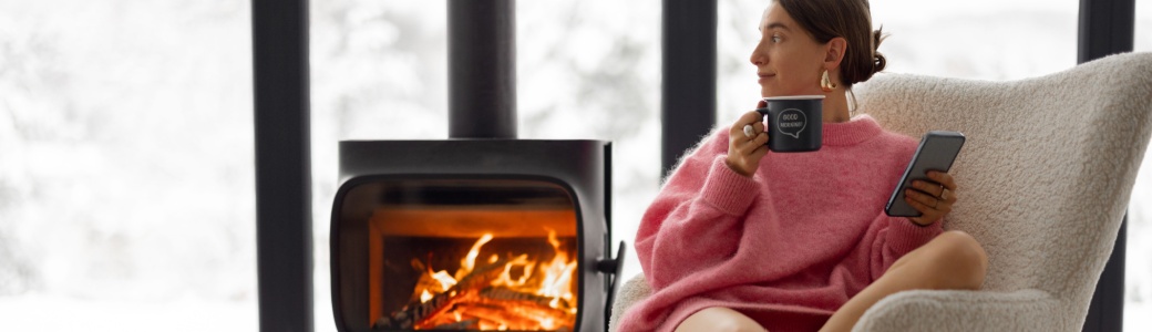 Woman sitting in a chair with a wood fire behind her.