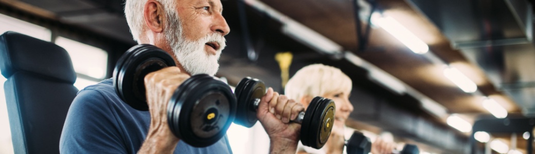 Two people in their 60s using weights in a gym.