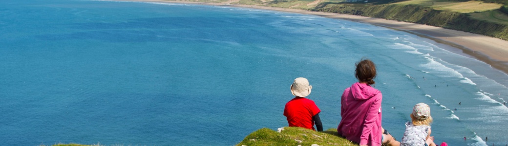 A family sitting on a clifftop overlooking a beach.